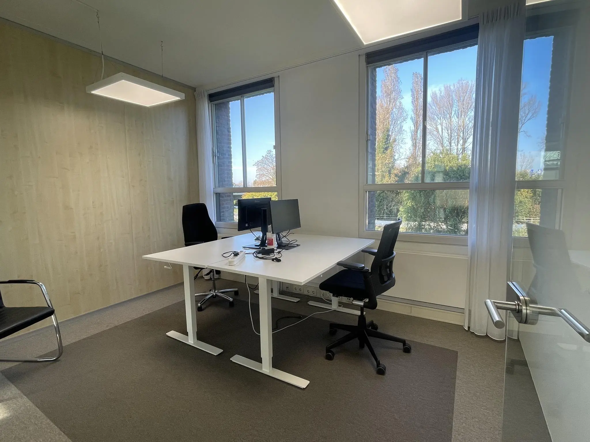 Modern kantoor met twee bureaustoelen, een bureau met computers en grote ramen aan de Jan Leentvaarlaan.